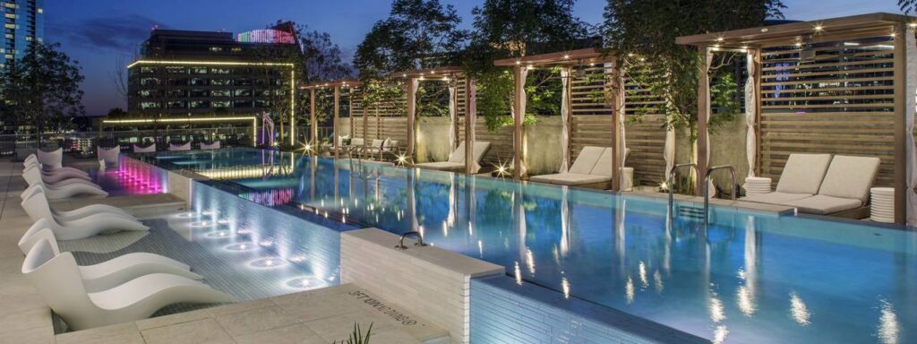 Atelier Dallas Apartments offers a luxurious downtown living experience with a rooftop pool adorned with lounge chairs and enchanting lighting at night. 
