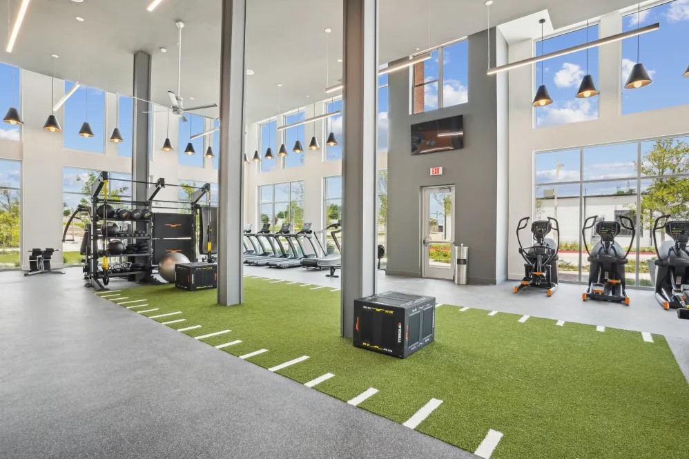 Modern apartment gym at The Margaret at Riverfront in Dallas Texas with high ceilings, cardio equipment, and turf workout area near Uptown Dallas