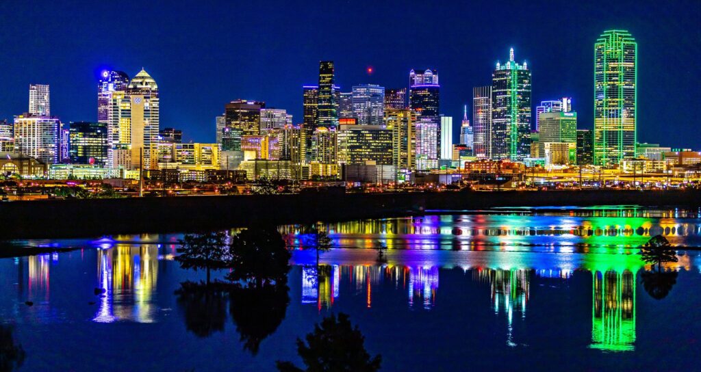 Dallas Texas skyline at night with colorful city lights reflecting on water near Downtown and Uptown Dallas.
