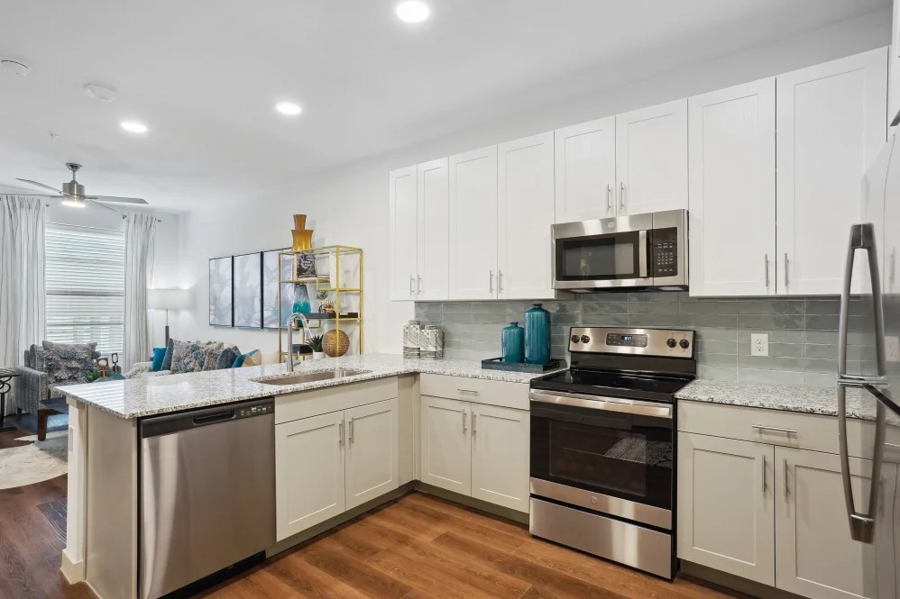 Modern apartment kitchen at The Margaret at Riverfront in Dallas Texas with white cabinets, stainless steel appliances, and open layout near Uptown Dallas.